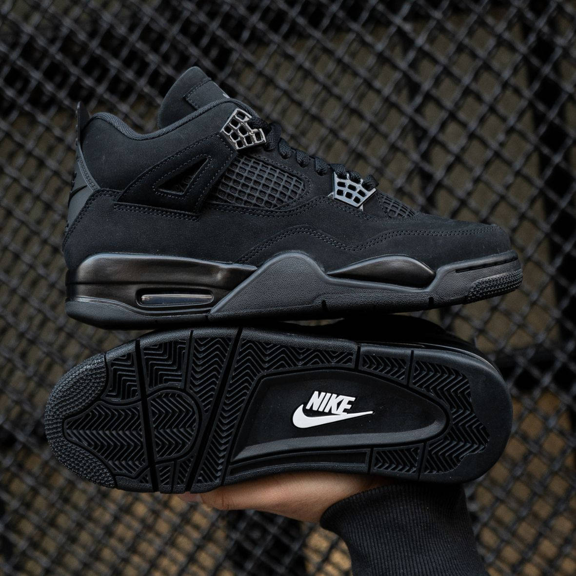 Air Jordan 4 Black Cat 2025 side and outsole angle in hand with black fence backdrop