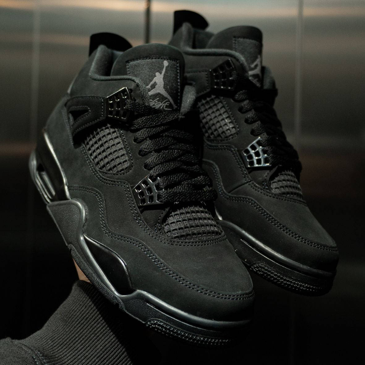 Air Jordan 4 Black Cat 2025 pair in hand shot with dim lighting in elevator with brushed metal backdrop