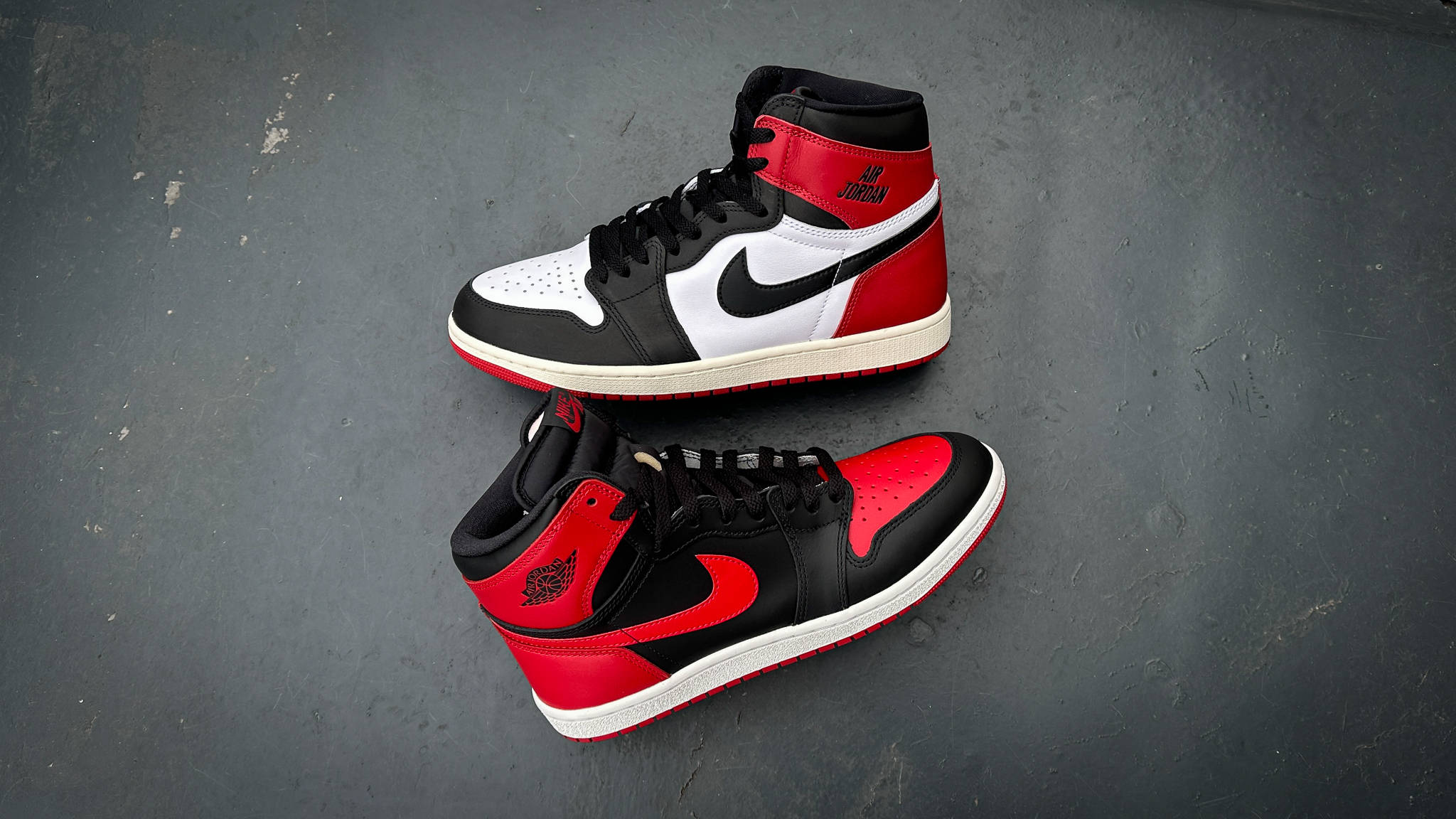 jordan 1 bred '85 lay down against a dark grey background next to the Air Jordan 1 Reimagined Black Toe retro