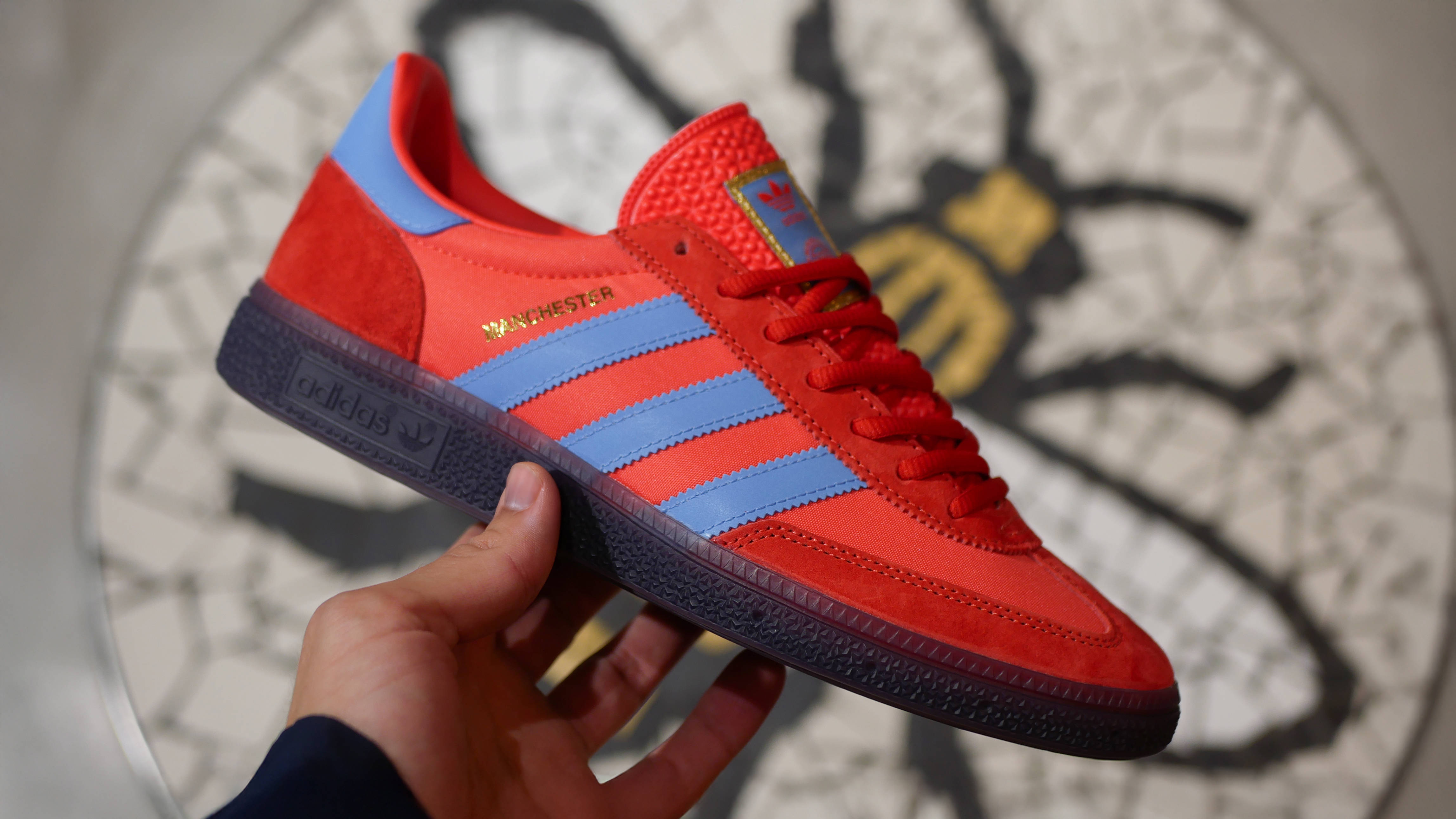 Size? adidas Manchester City Series 2025 in-hand shot against a bumblebee emblem mosaic from size manchester store