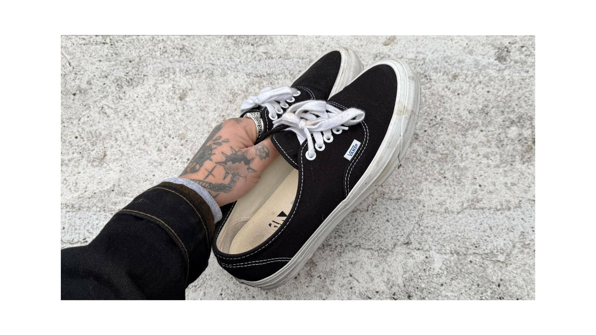 Vans DX44 black colourway in hand shot tattooed hand against white concrete backdrop