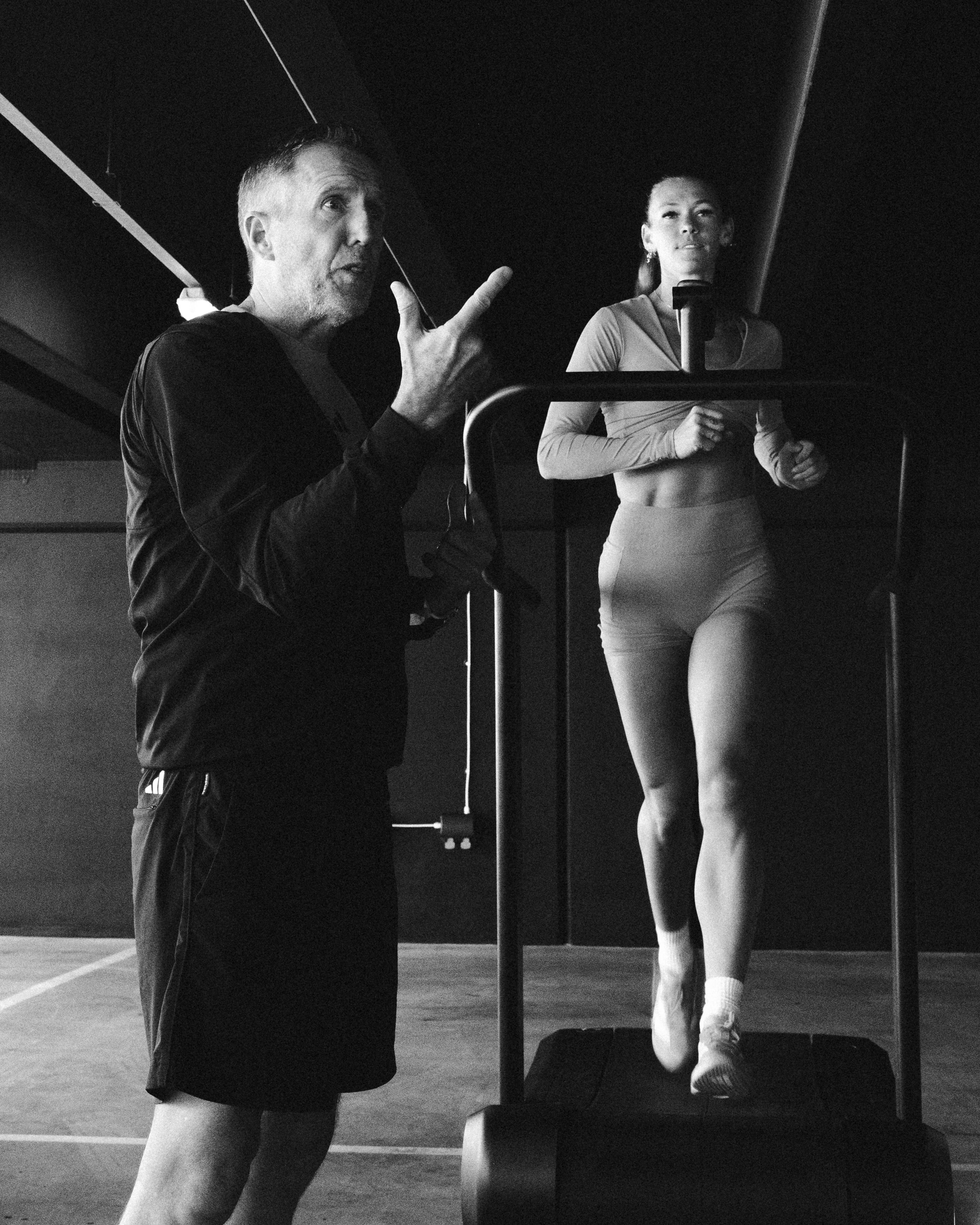 man teaching hybrid athlete female on treadmill black and white