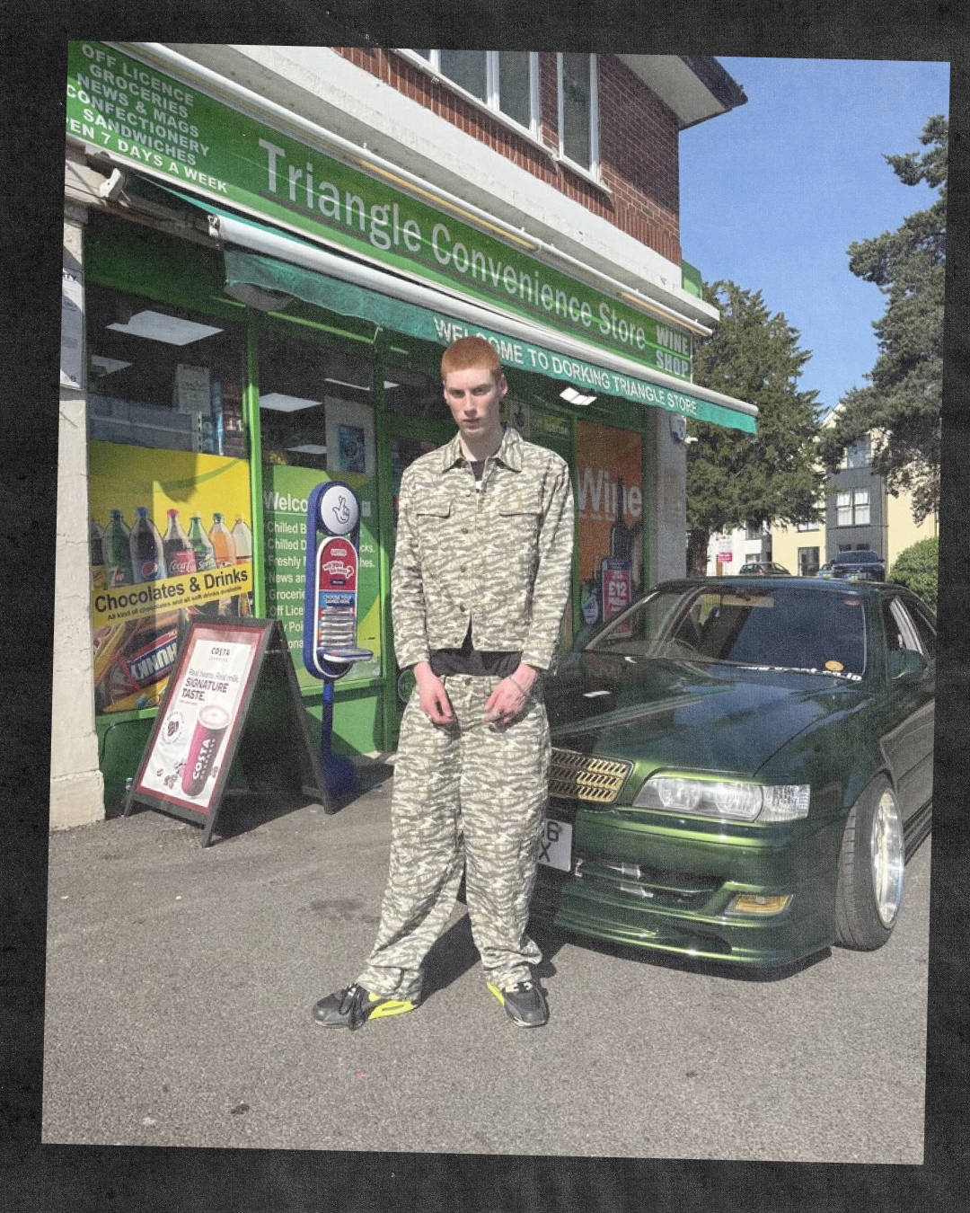 male model outside corner shop posing next to car in matching camo denim wearing nike air max 90s