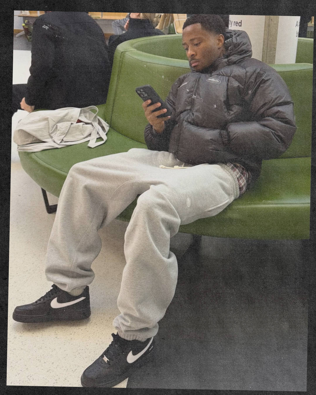 male model in jogging bottoms and corteiz puffer paired with black air force 1s with a white swoosh sat down on phone