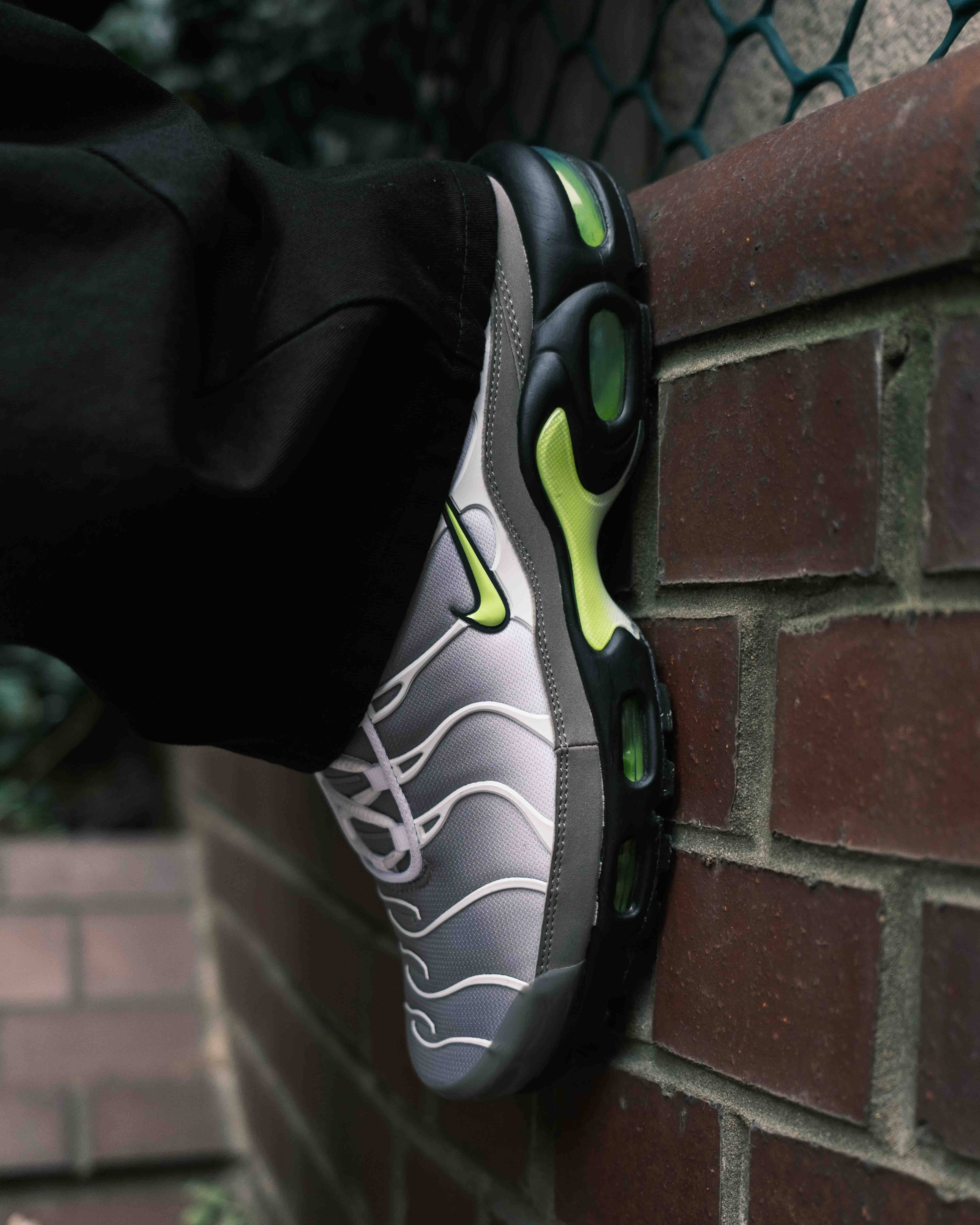 Nike Tn Neon kicked up and perched against brick wall