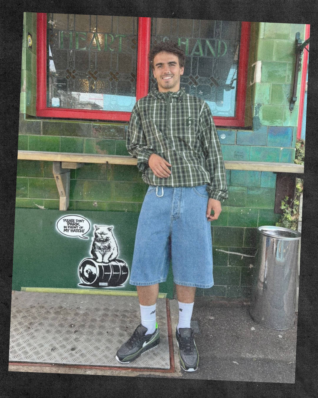 leaning pose male model wearing air max 90 mad pack in jorts and homegrown tartan jacket