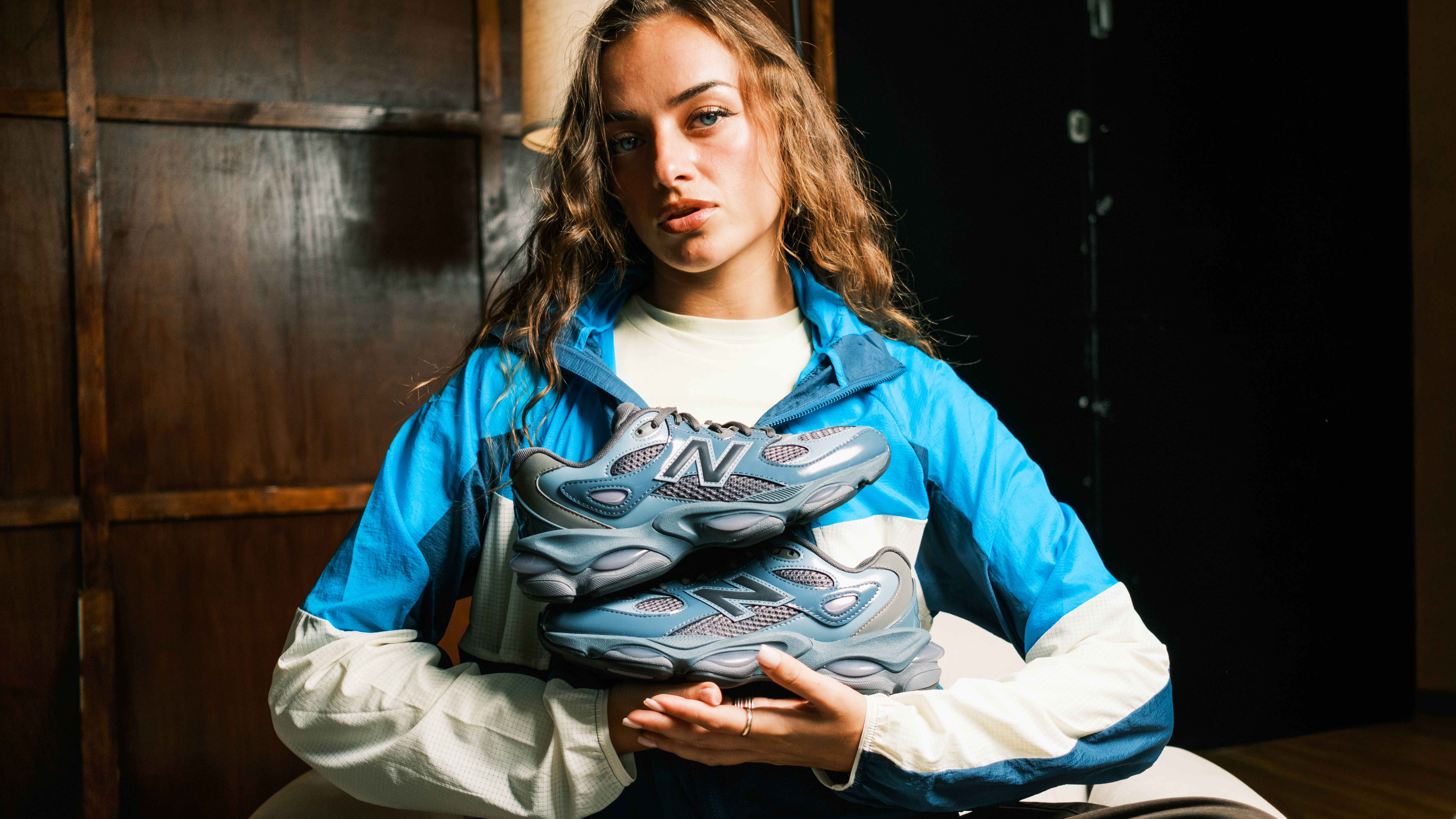 editorial model holding up a bundle of the new balance 983 wearing a sporty track jacket