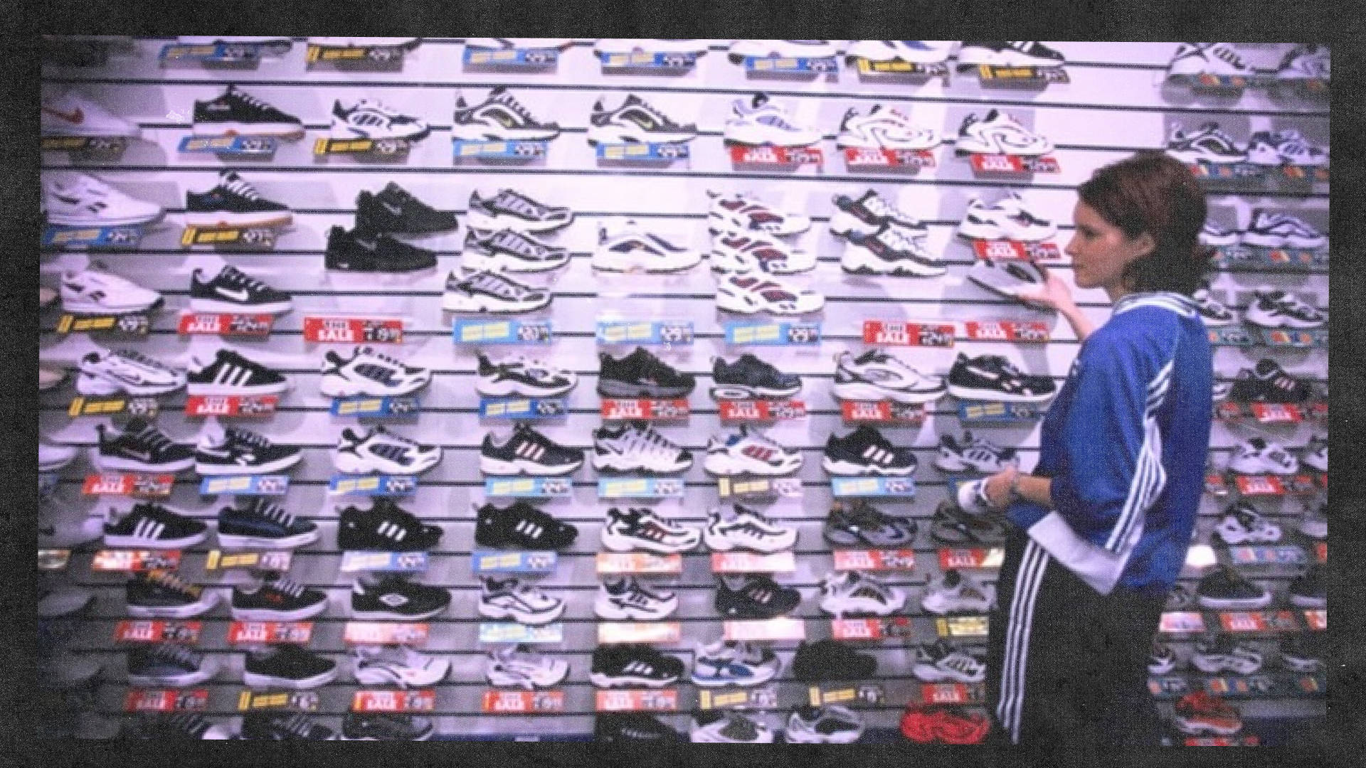 female sports shop employee stood by shoe wall from 1990s lots of mesh running silhouettes on the shelves